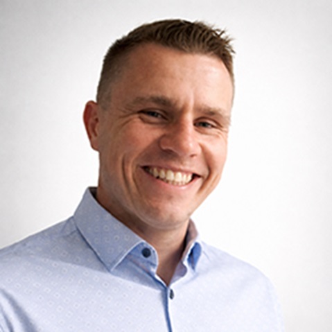 Osoba w jasnoniebieskiej wzorzystej koszuli, na jednolitym tle. Portret Marek Lewandowski.