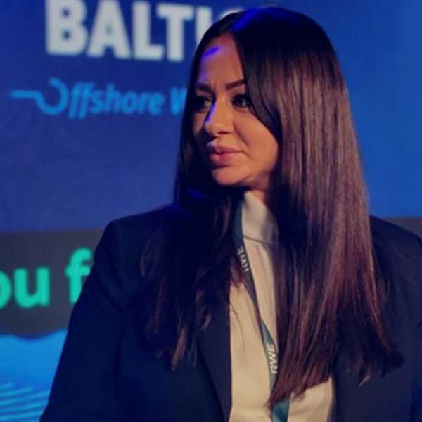 Osoba w garniturze stoi na scenie, na niebieskim tle z napisem 'Offshore Wind' i innymi tekstami.