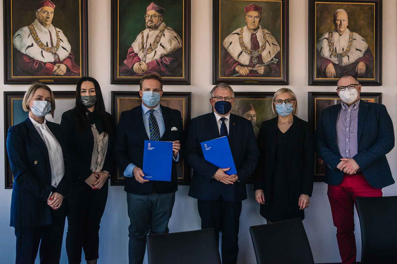 Group photo in a room with historical portraits. Various individuals holding documents in blue folders.