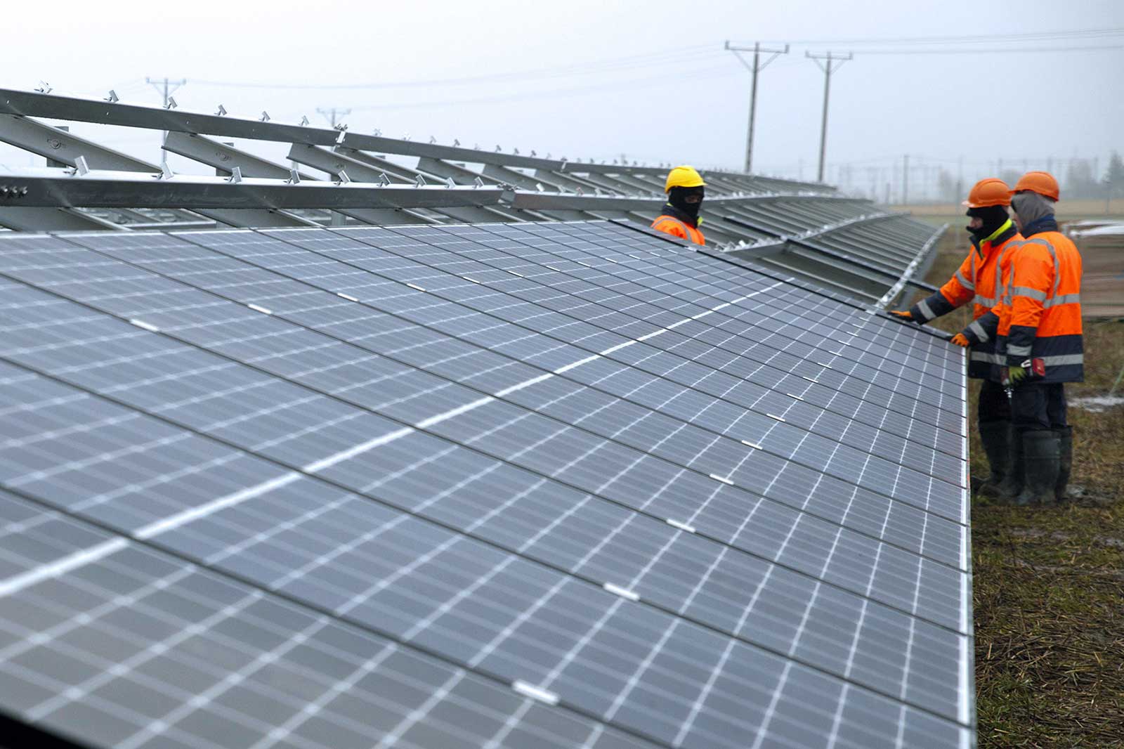 Workers in orange safety gear inspect solar panels in a cloudy environment.