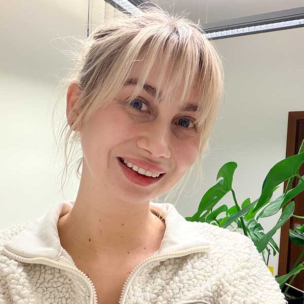 A person wearing a fluffy white jacket is seen in a well-lit room with a green plant in the background.