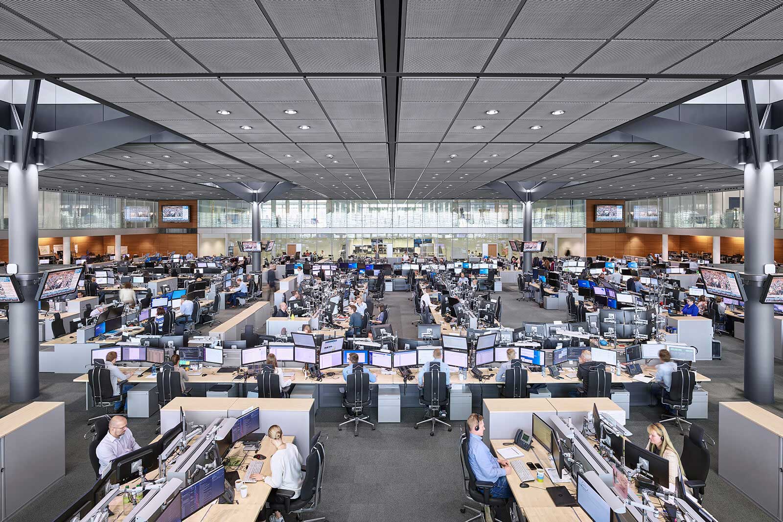 A modern office space filled with numerous workstations and computer monitors being used by staff.